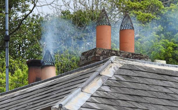 Chimney on household tiled roof with smoke coming out.